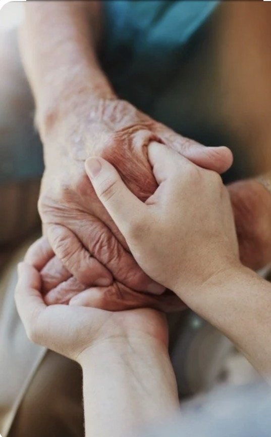 An elderly hand and a caregiver's hand holding one another.